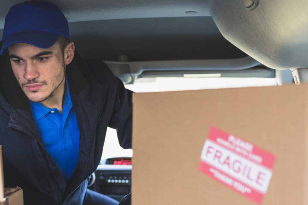 Man with the Van driver checking cartons at the back of the van labelled with 'Fragile' content